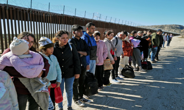 A group of immigrants are in a line outside.